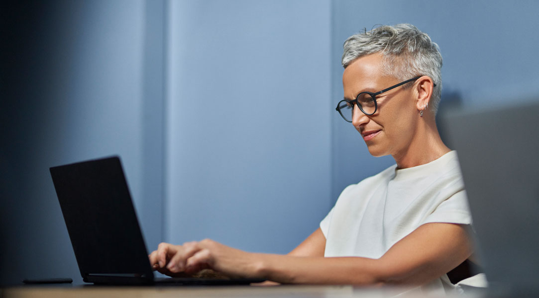 Eine Frau sitzt an einem Tisch und arbeitet an einem Tablet.