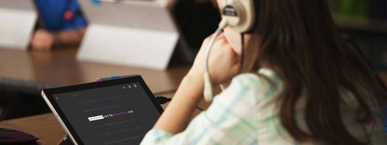 A girl wearing headphones using the immersive reader on her Microsoft Surface computer